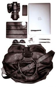 Top view of a traveler's bag laid out consisting of macbook air, pens, cards, DSL camera, ipad, water bottle, sunglass, and bag